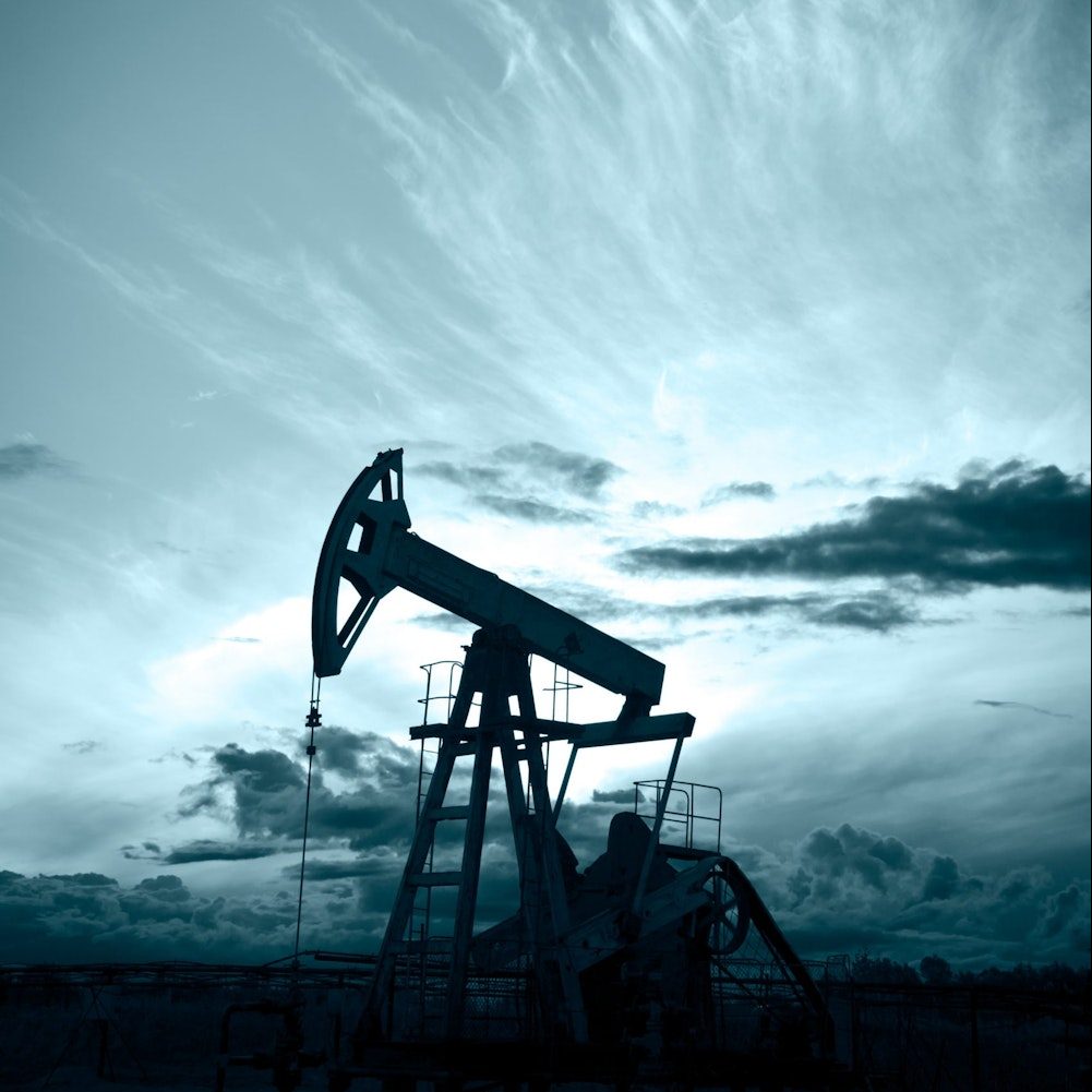 Silhouette of oil pump on background of blue-colored sunset